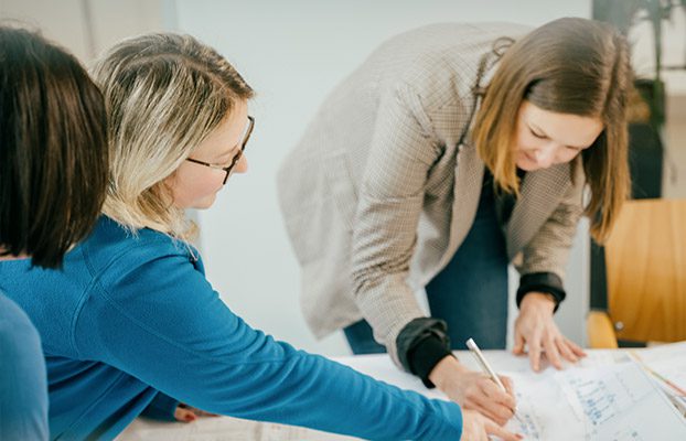 Zwei Personen, ein Berater und ein kommunaler Mitarbeiter, besprechen am Tisch Unterlagen für eine Ausschreibung im Bereich Wasserwirtschaft.